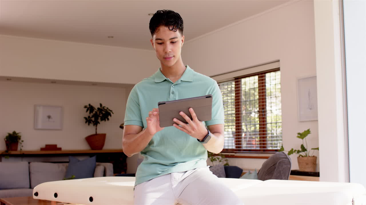 Using tablet, young man in casual attire working in modern home office
