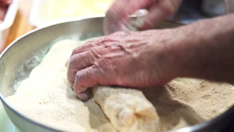 close up of man hands breading a raw steak with bread crumbs from metal bowl