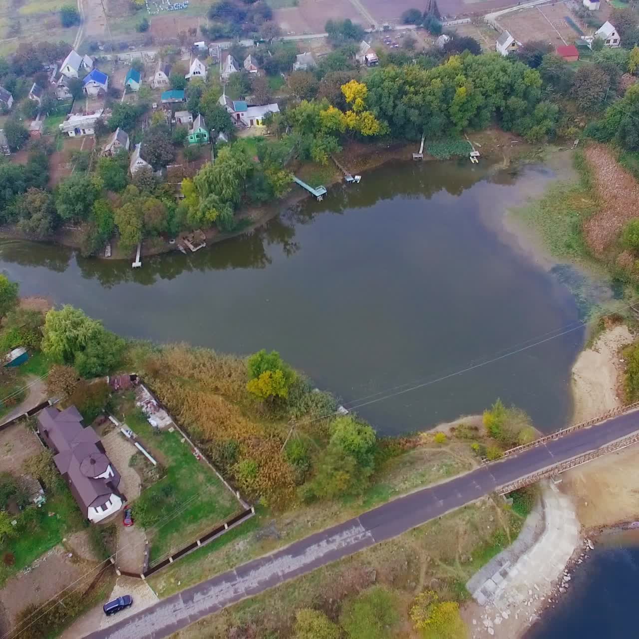Rural houses built around the ponds in countryside. Agricultural fields at backdrop. Aerial perspective on grey cloudy day