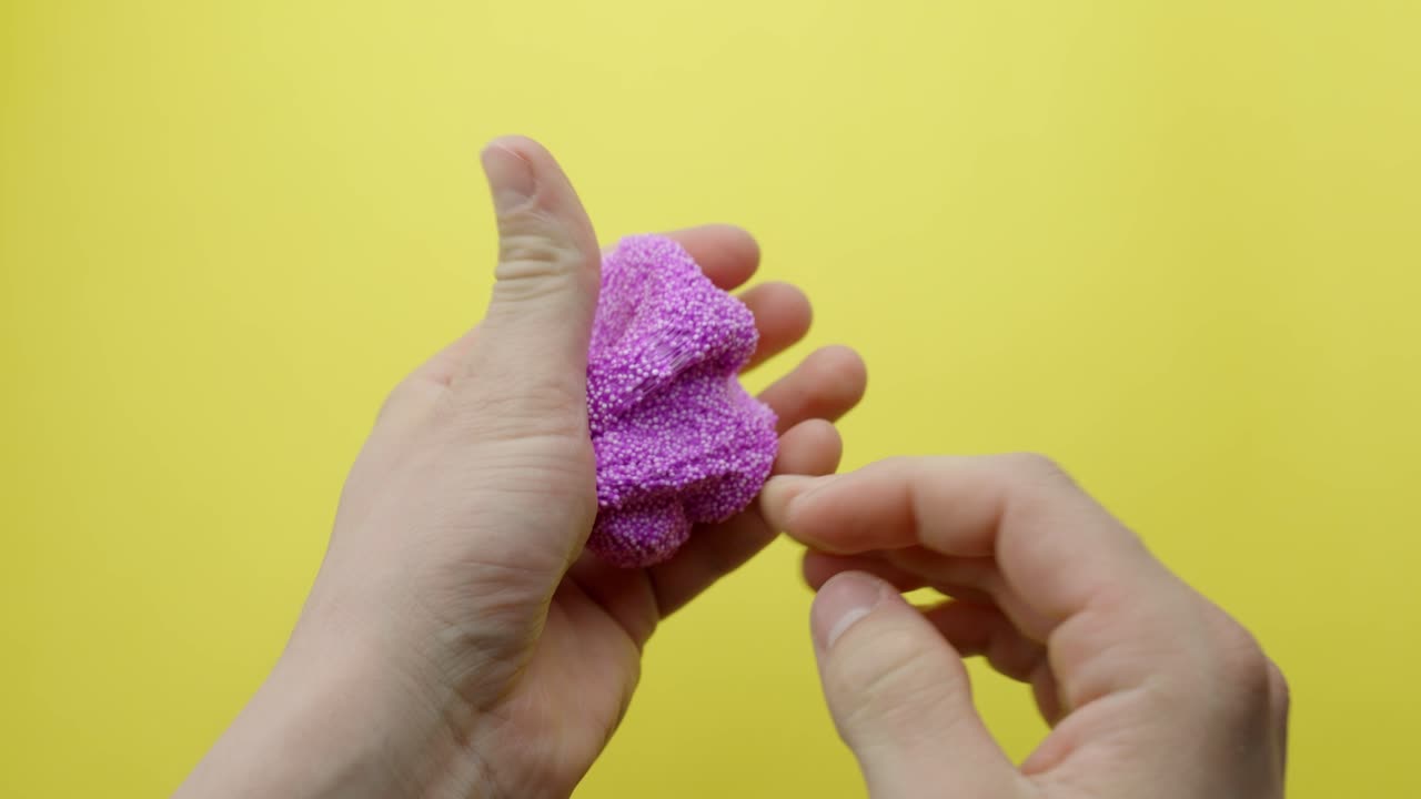 Pink Floam slime is slowly kneaded for ASMR against a vibrant yellow background, creating satisfying sounds.