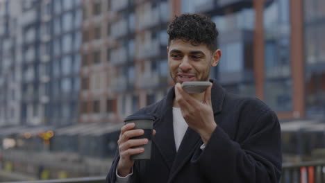 young man talking on speakerphone with coffee cup in city