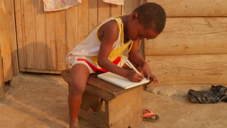 africa school education learning concept: young kid studying alone doing homework in remote poor african village