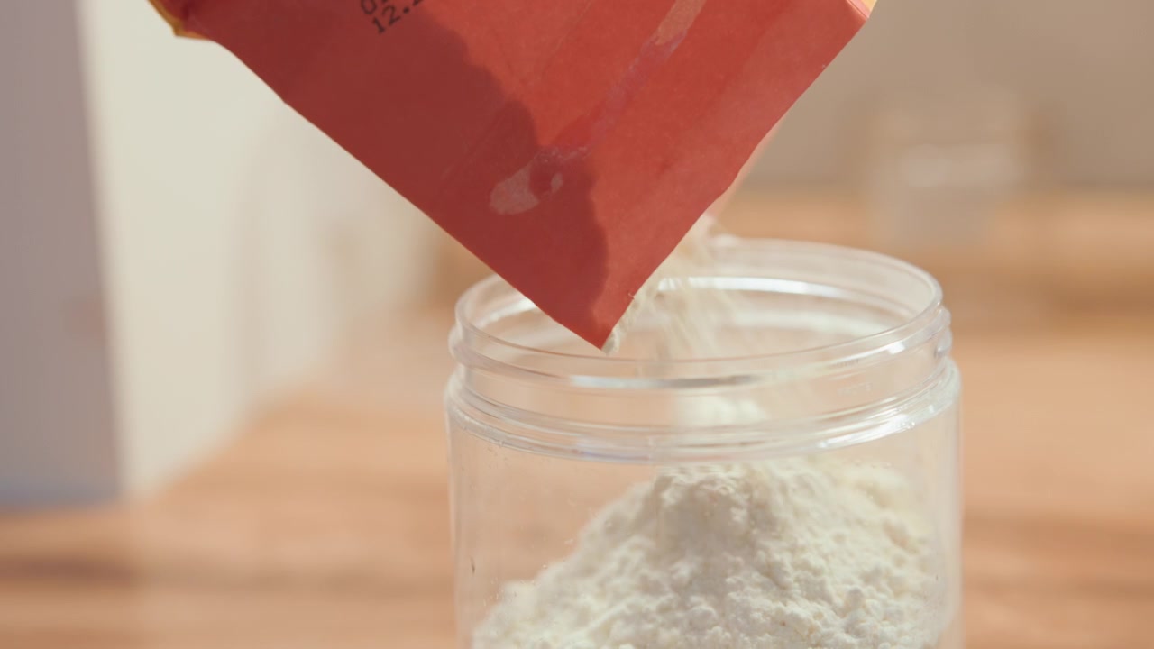 Primer plano de harina vertiéndose en un frasco durante una lección de repostería casera, un estudiante de repostería aprendiendo medición y técnica en una encimera de madera, luz natural cálida, un frasco de despensa ordenado enfocado, momento de práctica de receta.