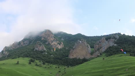 Paragliding-pilots-fly-paragliders-among-clouds-and-green-mountains.