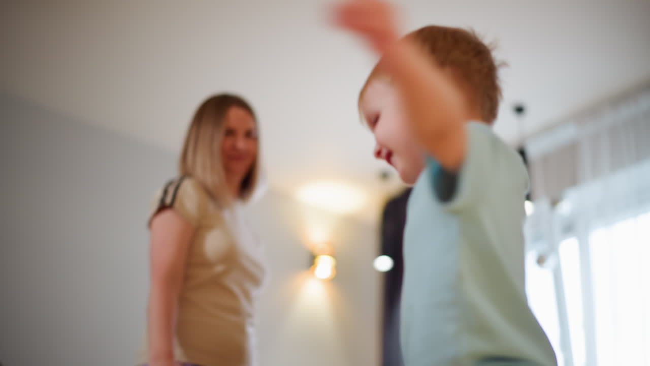 Child spreads arms in playful motion while mother watches with smile in cozy home interior, capturing energetic moment of joy, family connection, carefree activity, and positive bonding atmosphere indoors