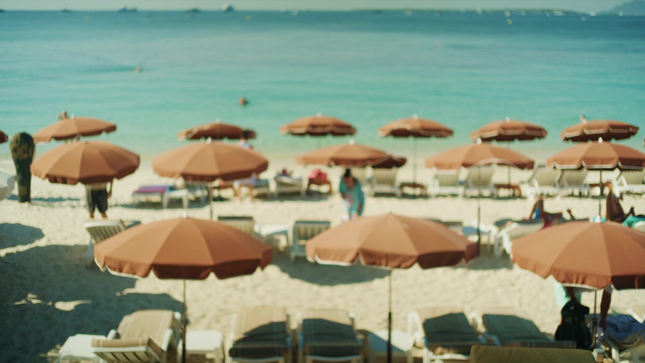 Ampia vista di una fila di ombrelloni marroni e lettini con persone che si rilassano in riva al mare, Cannes, Francia