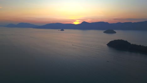 Tranquil-sunrise-with-radiant-beams-reflecting-off-the-calm-sea,-creating-a-picturesque-silhouette-of-islands-against-the-morning-sky