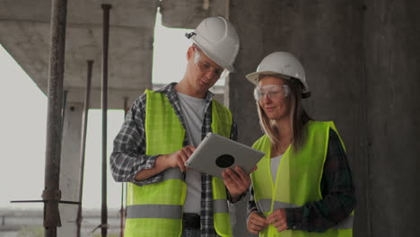 Professional-engineers-in-safety-vests-and-helmets-working-with-digital-tablet-and-blueprints