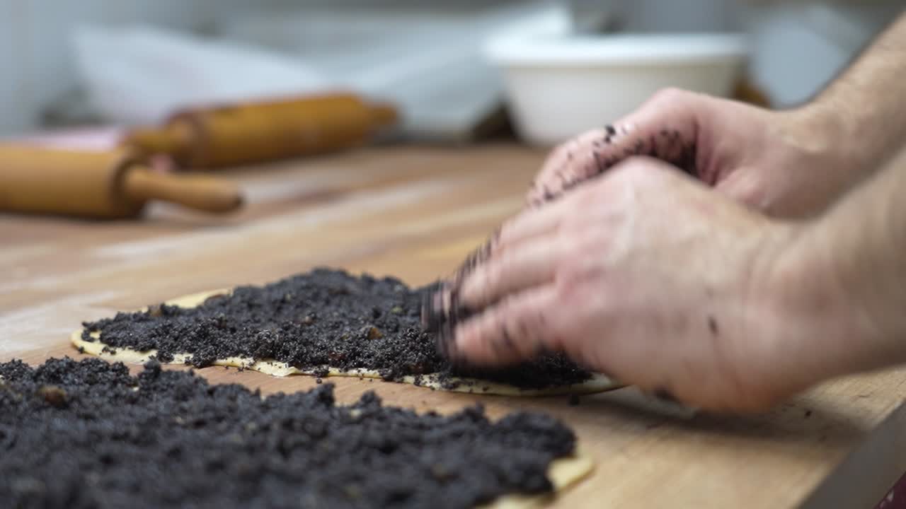 primer plano de manos extendiendo semillas de amapola llenando uniformemente la masa mientras se prepara el pastel de navidad húngaro bejgli
