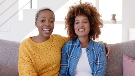 Portrait-of-happy-diverse-female-lesbian-couple-having-video-call-in-living-room-in-slow-motion