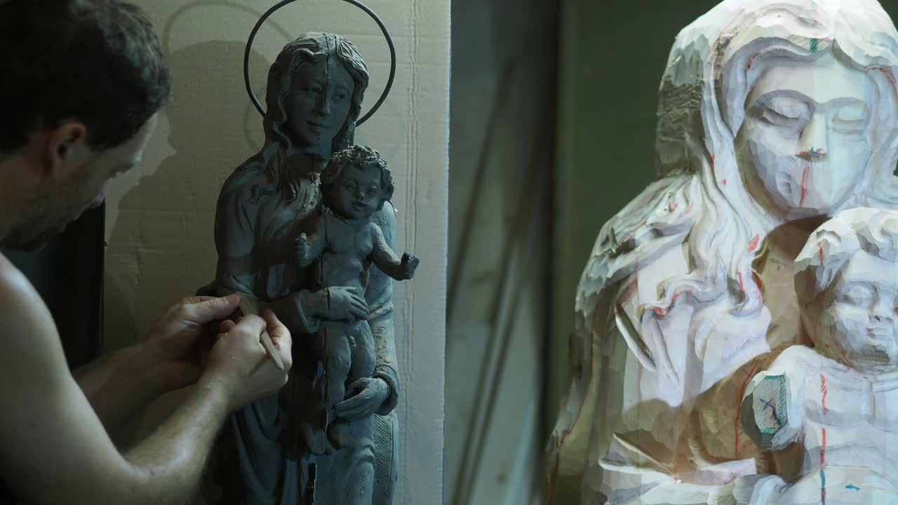 Artisan meticulously carves religious Madonna and Child clay smaller scale model sculpture in studio creating sacred devotional artwork with skill and tradition