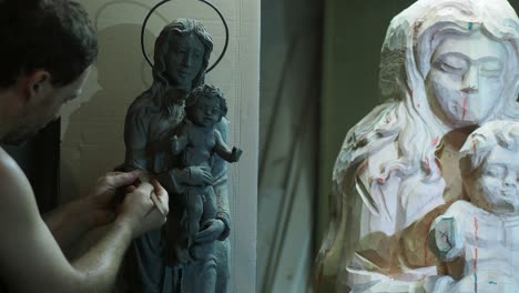 artisan meticulously carves religious madonna and child clay smaller scale model sculpture in studio creating sacred devotional artwork with skill and tradition
