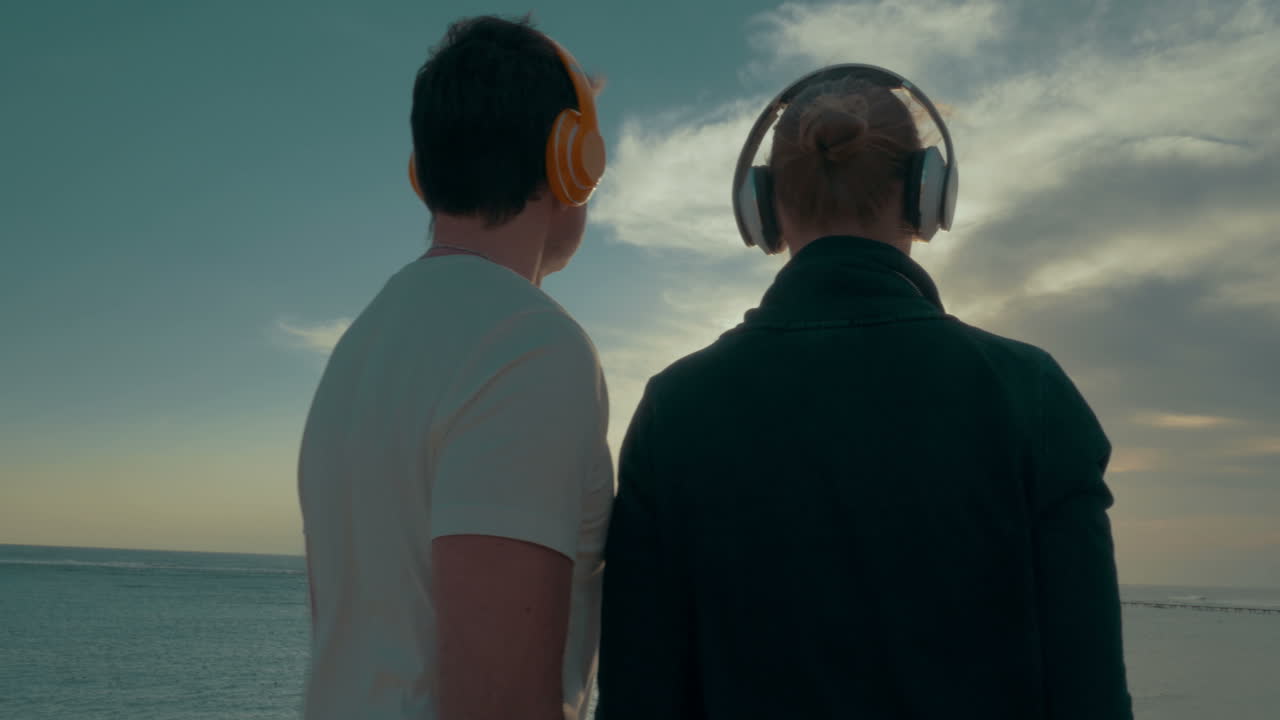 una pareja joven con auriculares disfrutando de la escena del mar y el cielo.