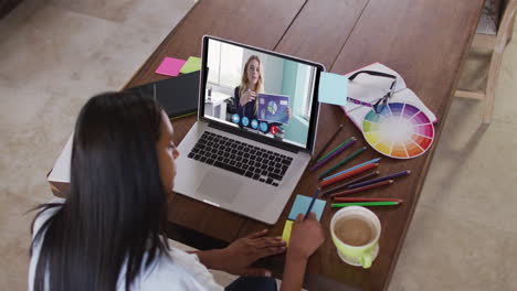 mujer caucásica usando una computadora portátil en videollamada con una colega y tomando notas