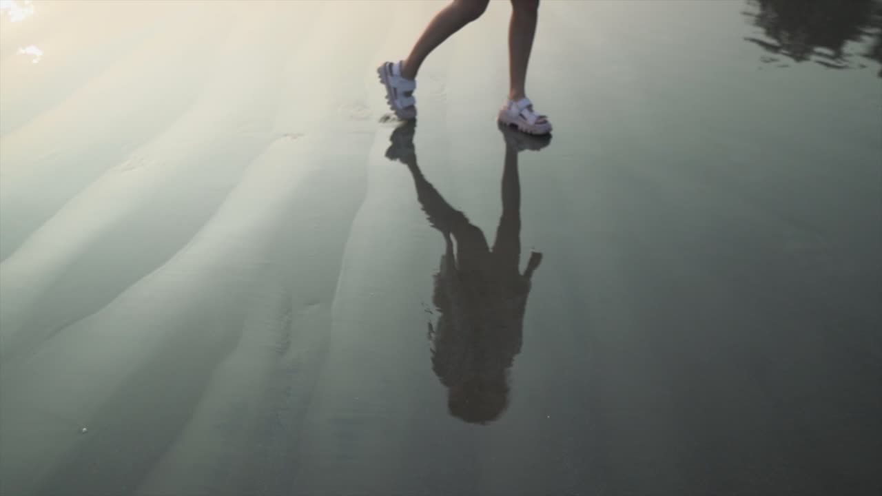 reflejo de silueta de una mujer joven caminando por la costa del océano, en una playa tropical de arena, al anochecer