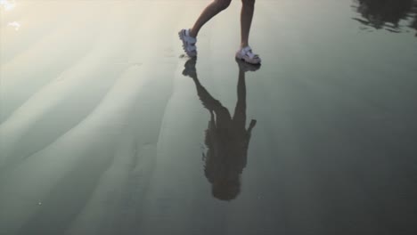 silhouette reflection of a young woman walking on the ocean shoreline, on a sandy tropical beach, at dusk