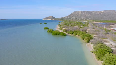 Drone-Shot-Flying-Over-Shoreline-Turquoise-waters-with-Iconic-El-Morro-Mountain-National-Park-in-the-Distance,-Dominican-Republic