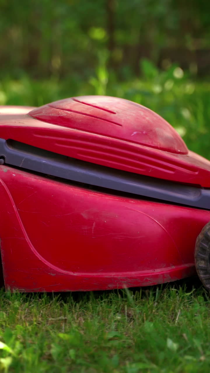 Grass trimming with electric lawn mower. Mowing the lawn grass in the garden. Garden work in summertime. Vertical video