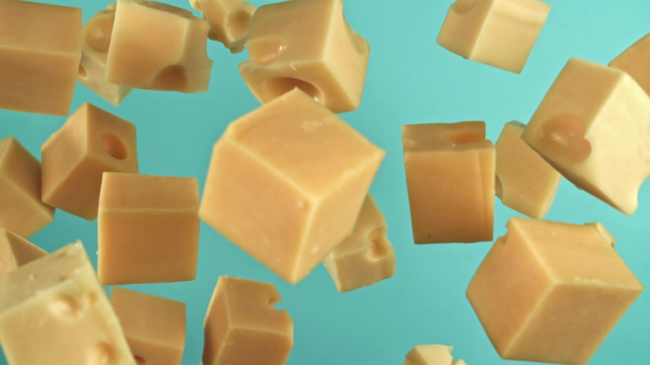 Cubes de fromage tombant au ralenti extrême sur fond bleu