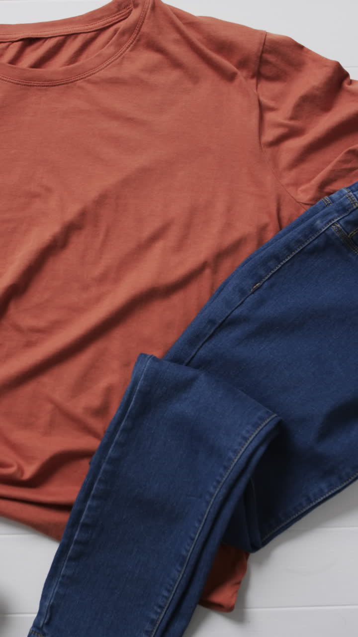 Vertical video of orange t shirt, denim trousers, shoes and copy space on white background