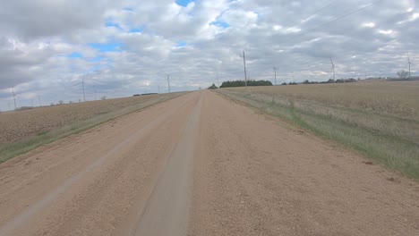 point of view driving on a straight stretch of graveled road, past harvested fields