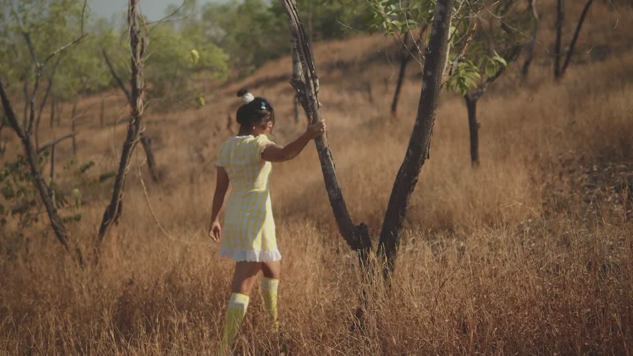 mujer bonita con vestido amarillo moviéndose entre los árboles en medio de la hierba en un hermoso día soleado