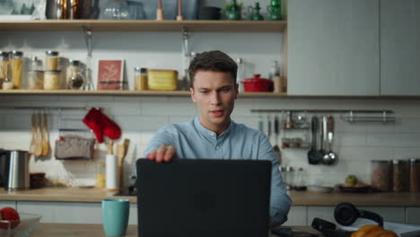 hombre termina una reunión en línea cerrando una computadora portátil bebiendo café en la cocina de cerca.