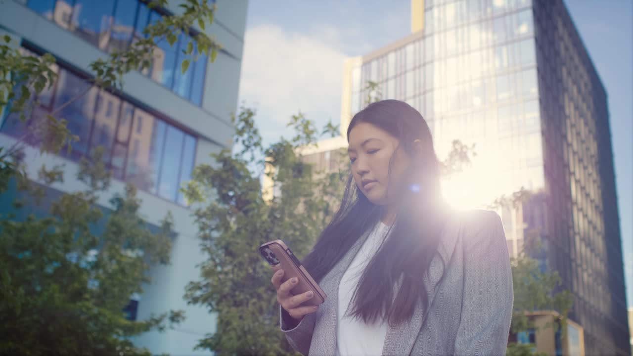 mujer china de negocios caminando por la ciudad y usando el teléfono