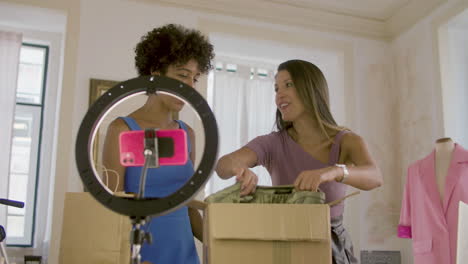 two female friends unpacking boxes with clothes, recording video