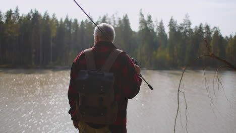 fisher is viewing lake in forest choosing place for fishing and enjoying nature in autumn season back view of person