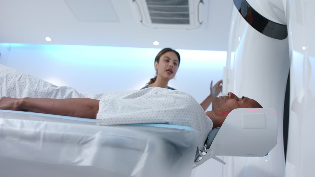 African American tech with male patient, using scanner panel after positioning at gantry for scan