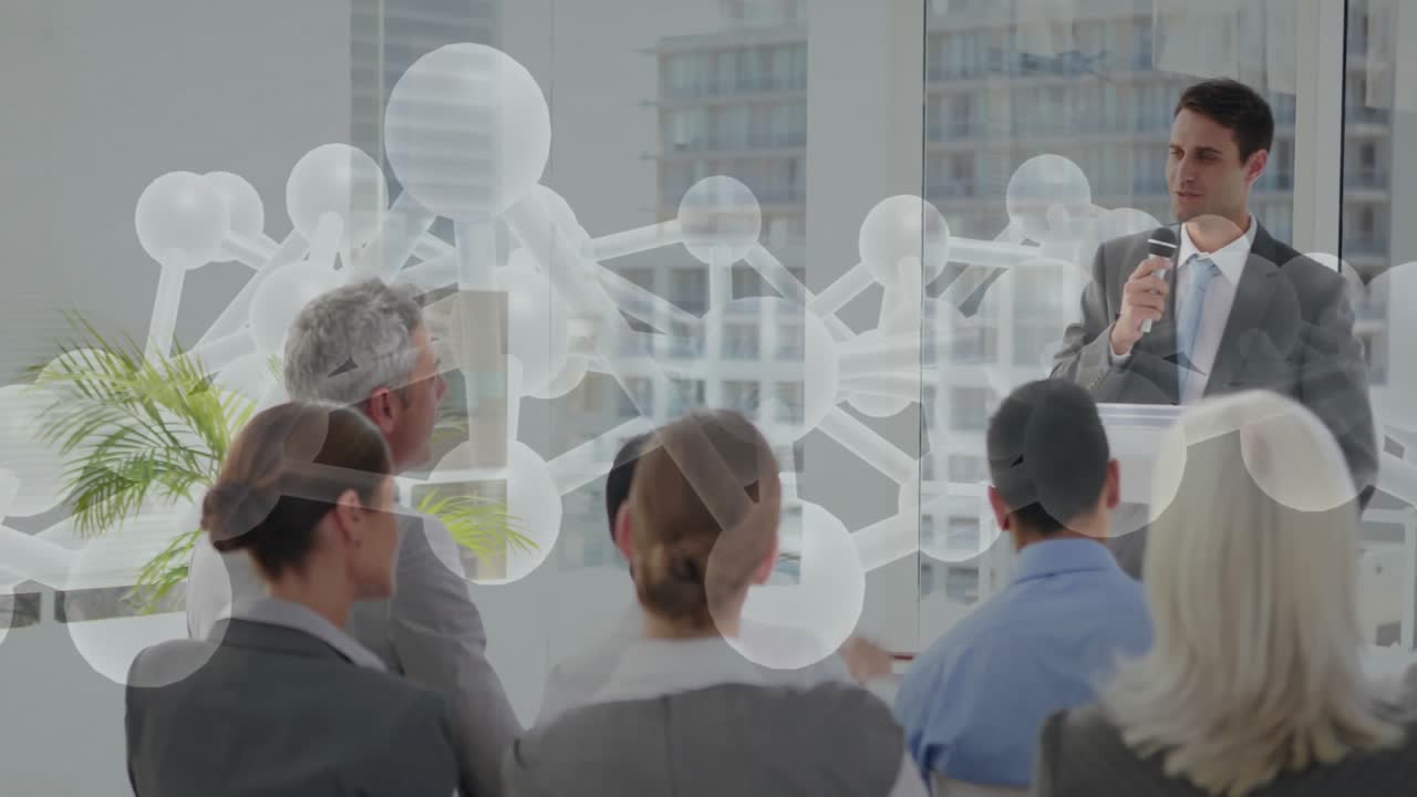 Zakelijke presentator gebruikt microfoon op een podium met publiek dat handen opsteekt en moleculaire overlay.
