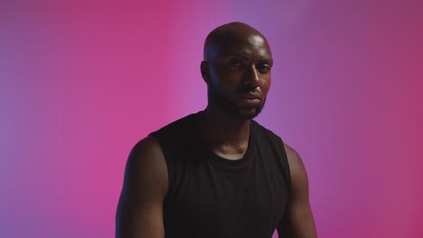 retrato de estudio de un atleta masculino con chaleco deportivo contra un fondo iluminado de color rosa y azul