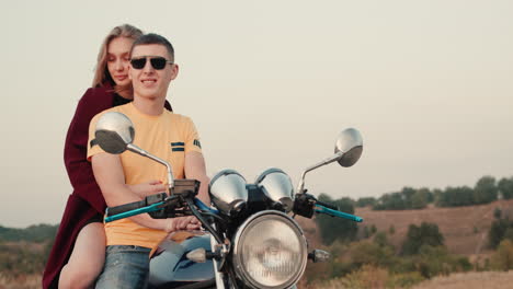 romantic couple sit on a motorcycle and admire the sunset