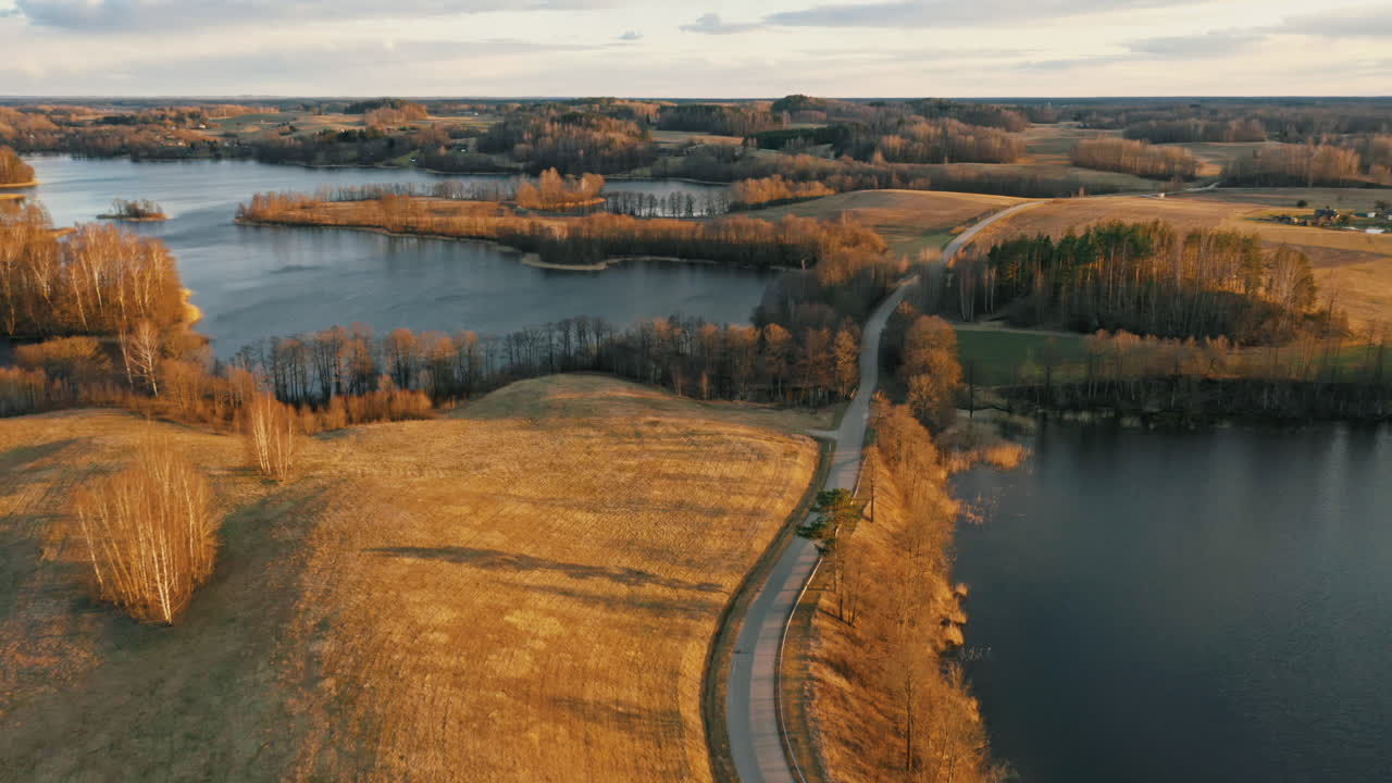 Narrow wild road between two lakes visible. Drone footage at evening.