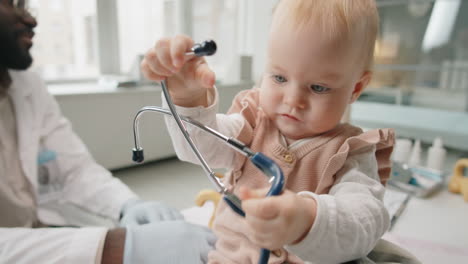 baby playing with stethoscope while mom talking with pediatrician