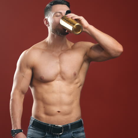 muscular sportsman in red studio. smiling bodybuilder mixing flask and drinks protein cocktail indoors. shirtless athlete with trained body.
