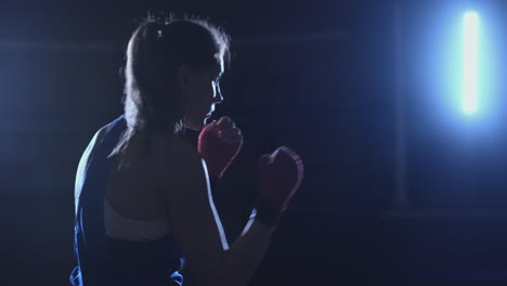 A-beautiful-woman-boxer-trains-in-a-dark-gym-and-works-out-punches-in-slow-motion.-side-view.-Steadicam-shot