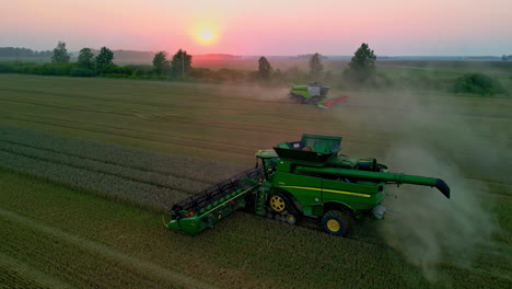 Luftdrohnenaufnahme-über-Einem-Grünen-Mähdrescher,-Der-Auf-Einem-Reifen-Maisfeld-Erntet,-Während-Sich-An-Einem-Herbstabend-Ein-Anderer-Mähdrescher-Im-Hintergrund-Bewegt