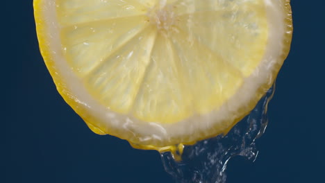 slow motion macro shot of flowing water from lemon slice on blue-black background