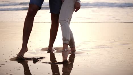Couple-of-lovers-man-and-woman-paint-with-their-feet-on-the-wet-sand-heart.-Cropped-footage-of-loving-couple-on-the-sea-coast.-Slow-motion