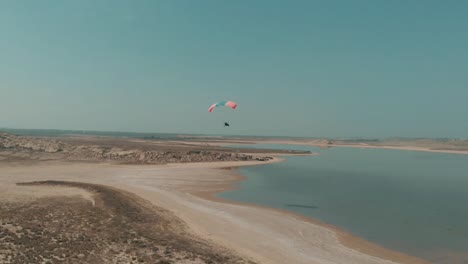 aerial view of motorised paraglider flying over arid coastline next to salt lake