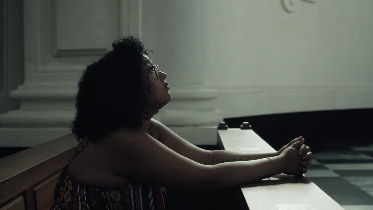 Beautiful young black woman praying for better times in the church.