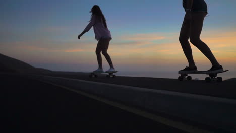 slow-motion footage showcases two friends in shorts skateboarding on a road during sunset. the mountains and a picturesque sky form an alluring backdrop