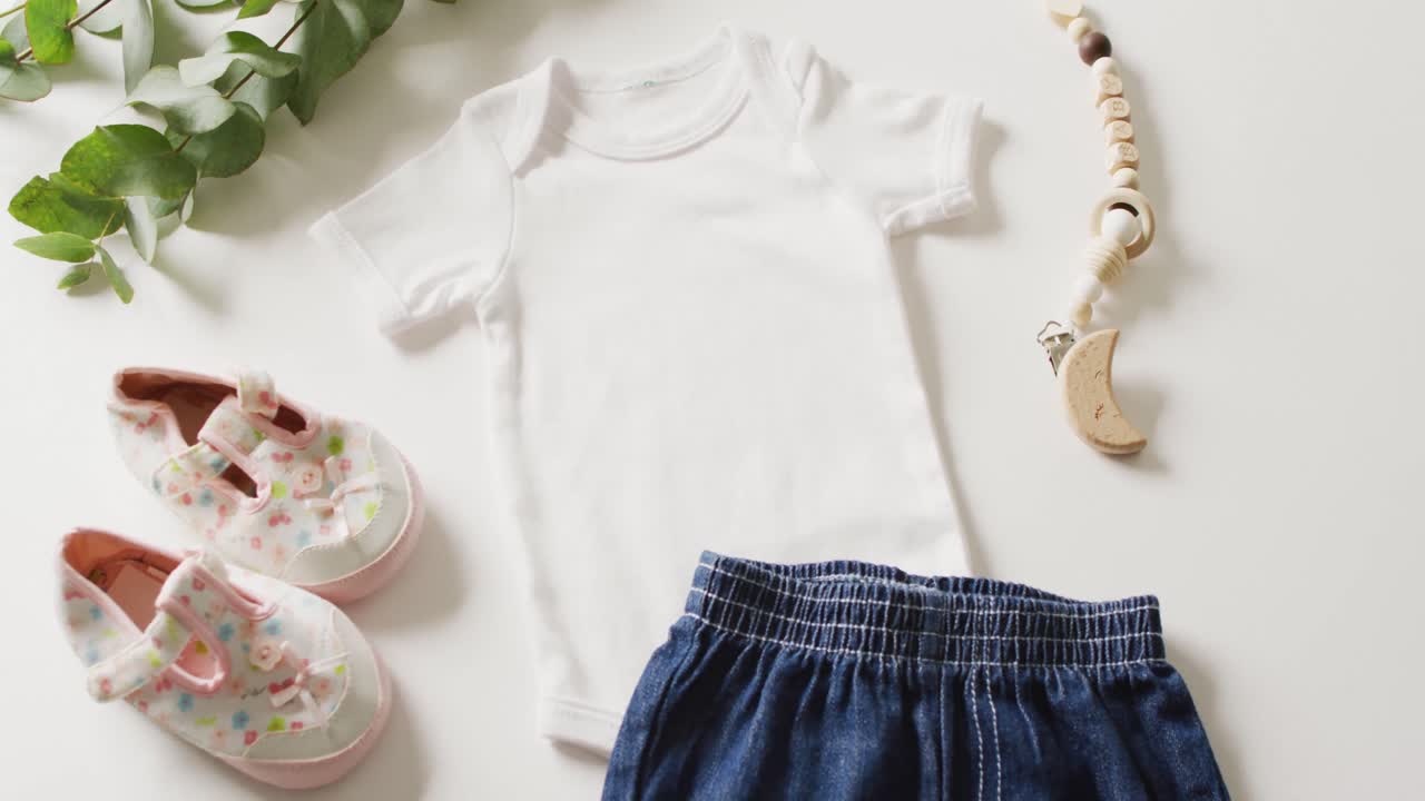 Video of close up of white baby grow, shoes and skirt on white background