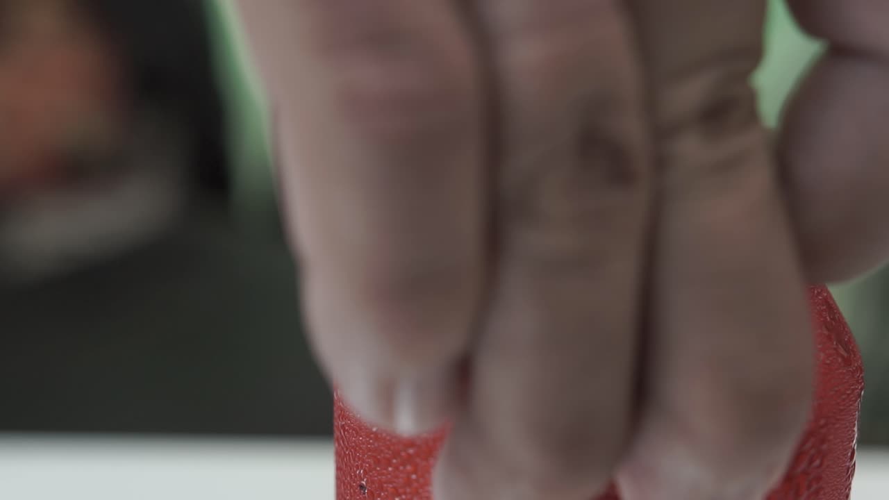 Close-up shot of hand opening cold red soda can covered in droplets under green light