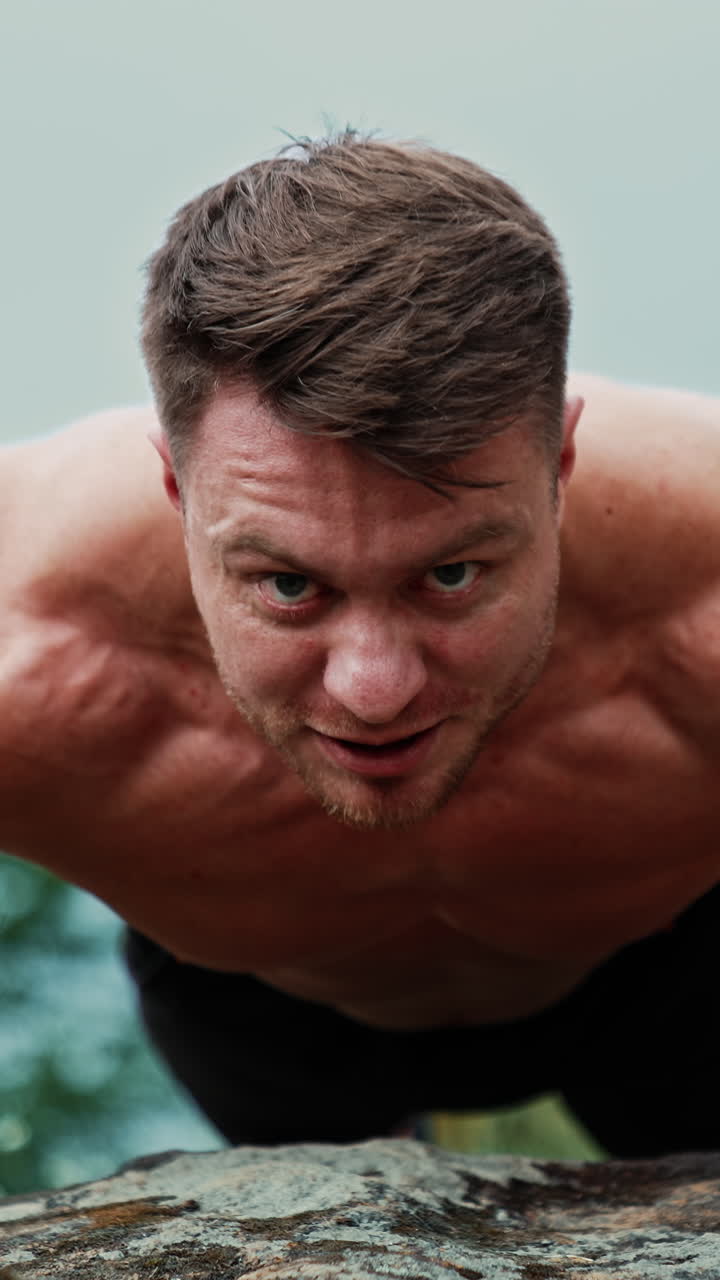 Front view of a strong man standing in plank. Athlete doing pushups on the rock. Blurred nature backdrop. Vertical video
