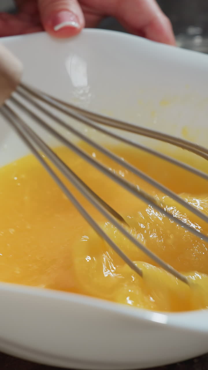primer plano de un chef batiendo huevos en un cuenco blanco en una encimera oscura, agarrando con la mano un batedor de madera, agitando las yemas en una textura suave para cocinar o hornear, la mezcla de huevos gira rápidamente
