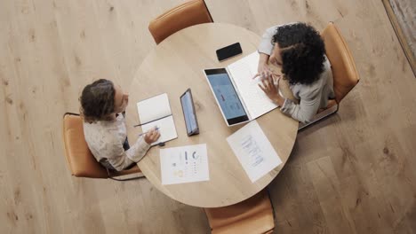 diverse female colleagues in discussion using laptop and tablet in office lounge, slow motion