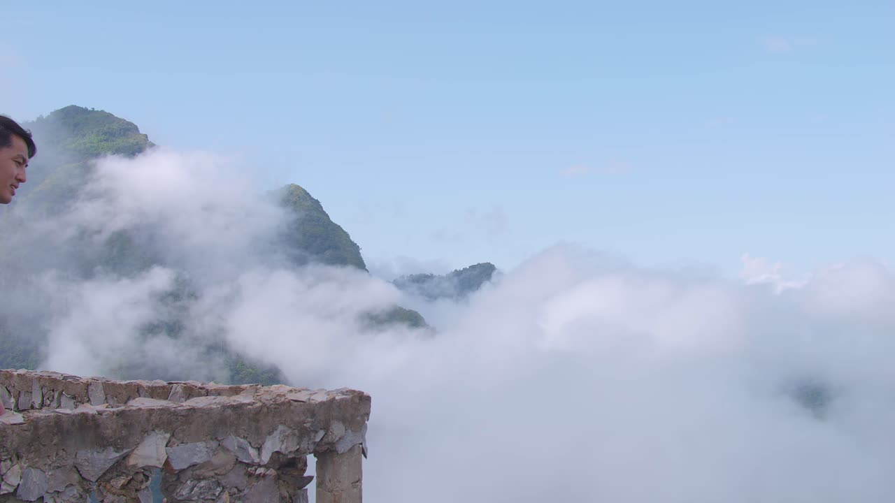 베란다 절벽으로 고 있는 아시아인 하이커 남성, 안개가 가득한 산 꼭대기의 아름다운 전망을 보고 있다.